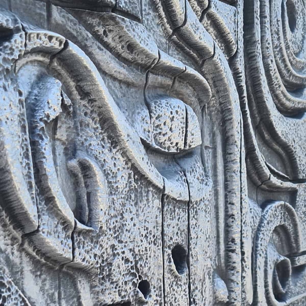 Primer plano de "Vivencias", un cuadro en relieve obra de A. Gea: la piedra, desgastada y ligeramente grisácea, cuenta su propia historia a través de surcos y curvas talladas con esmero. Los detalles geométricos se entrelazan, como recuerdos que se superponen en la memoria. La erosión -esas pequeñas marcas y hendiduras- no sólo profundiza las sombras; también parece acentuar el peso emocional de la pieza. Es curioso cómo algo tan frío como la piedra puede llegar a transmitir tanto, casi como si al pasar los dedos por esas cicatrices del tiempo pudieras sentir las huellas invisibles de vidas anteriores.